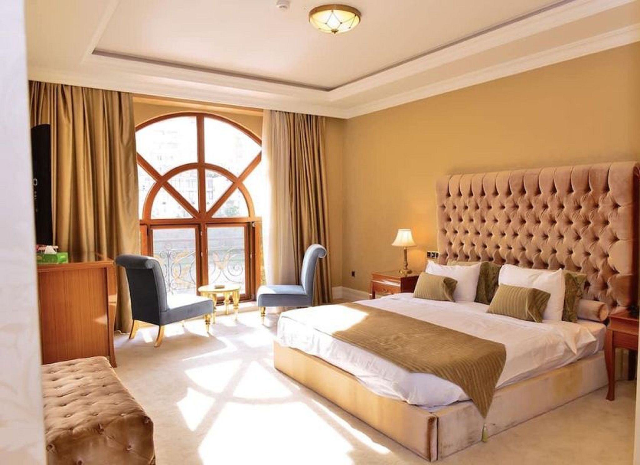 Ein Hotelzimmer mit einem großen Bett, zwei Sesseln, einem kleinen Tisch und einem Fenster mit Vorhängen.