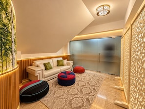 A modern living room with a sofa, ottomans, a patterned rug, and a wall-mounted light fixture.