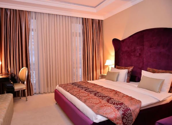 A hotel room with a large bed, a desk with a chair, and a window with curtains.