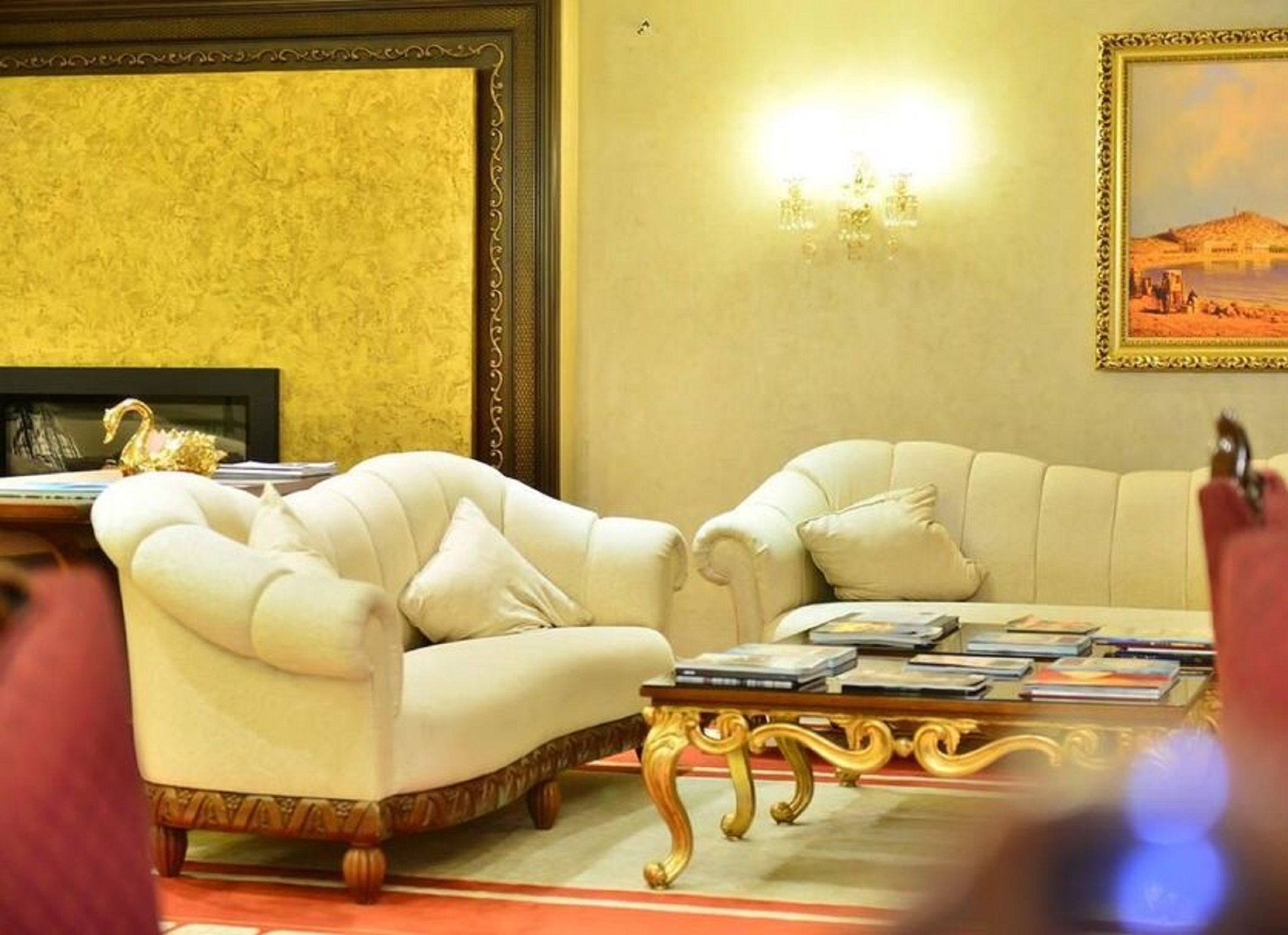 A room with two white armchairs, a coffee table with books, a wall-mounted light, and a framed picture.