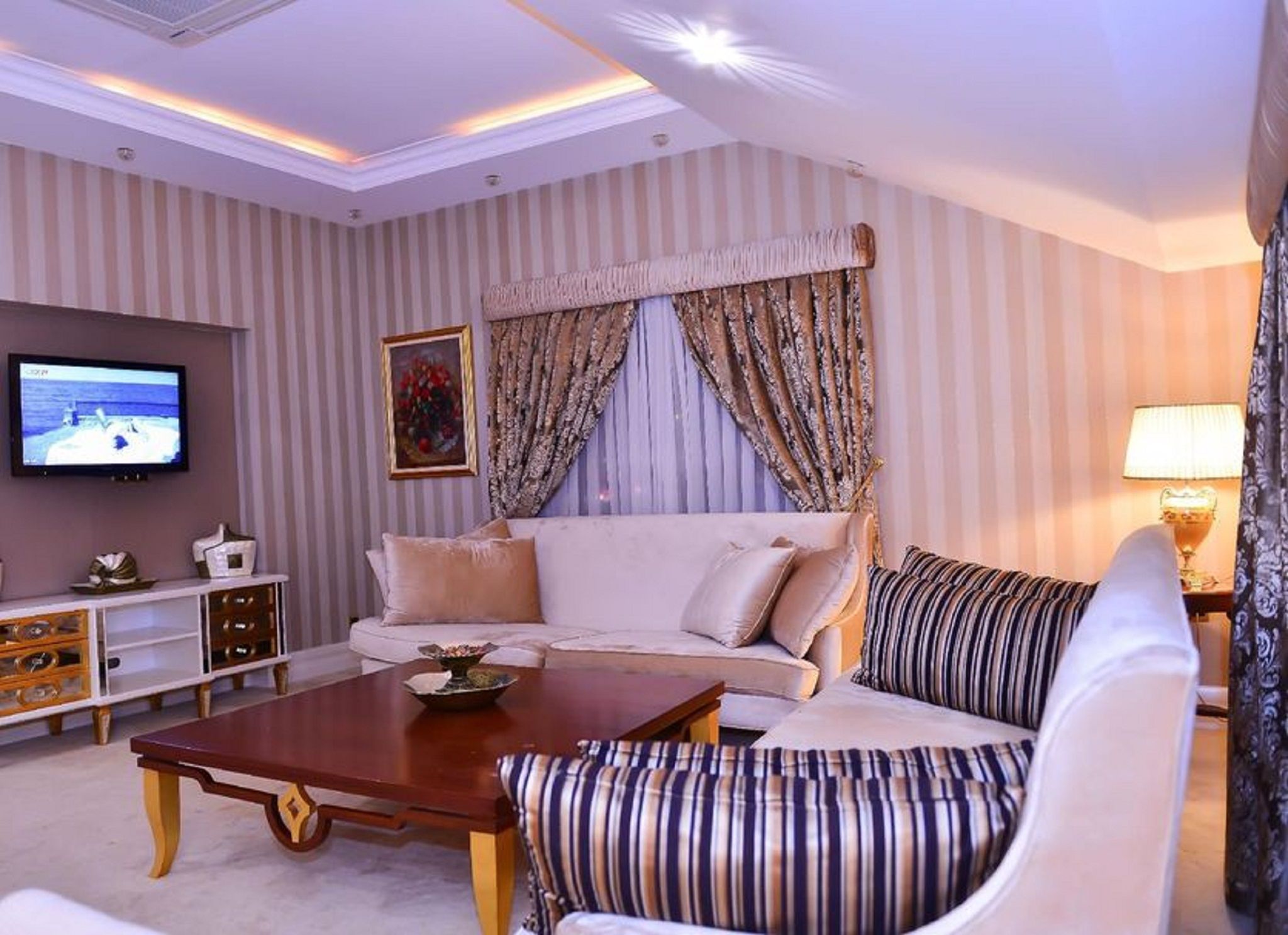 Habitación de hotel con sofá, una mesita de centro, televisión y cortinas a rayas.