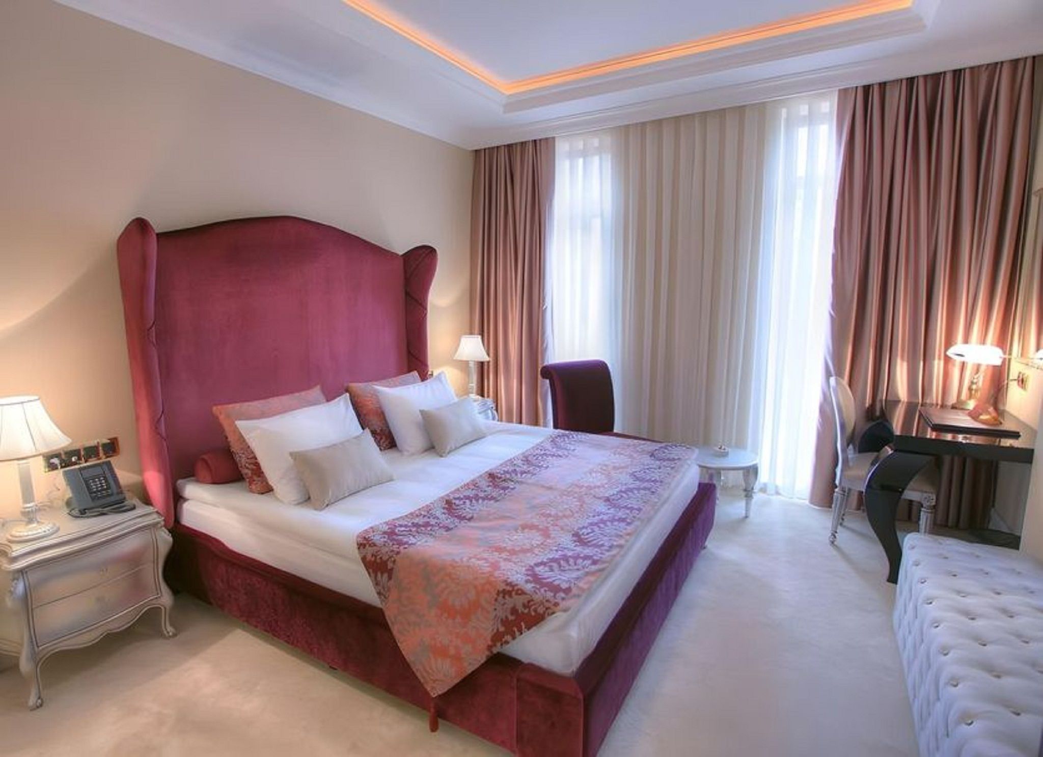 A hotel room with a large bed, a desk, a chair, and a bedside table with a lamp.