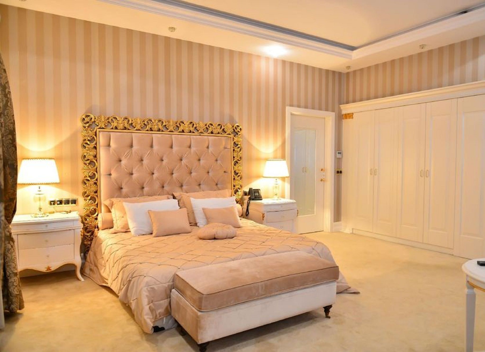 A bedroom with a large bed, two bedside tables, a wardrobe, and a door.