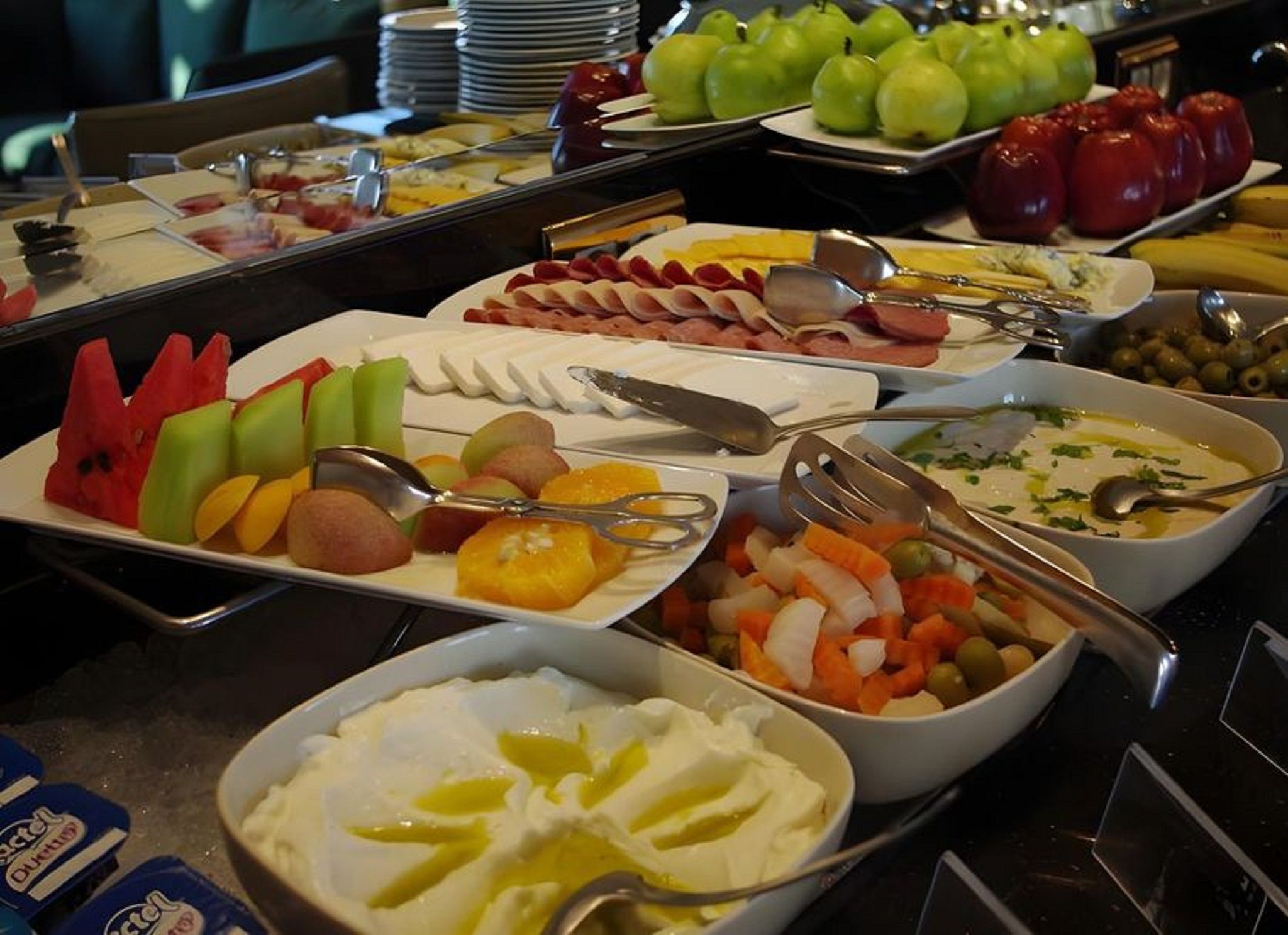 Un bufé con diversos alimentos, entre ellos frutas, verduras y salsas.