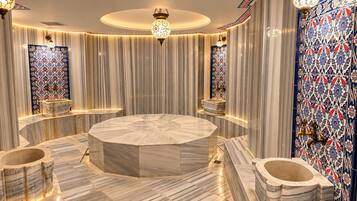 Un baño lujoso con un lavamanos central de mármol, múltiples dispensadores de toallas e iluminación decorativa.