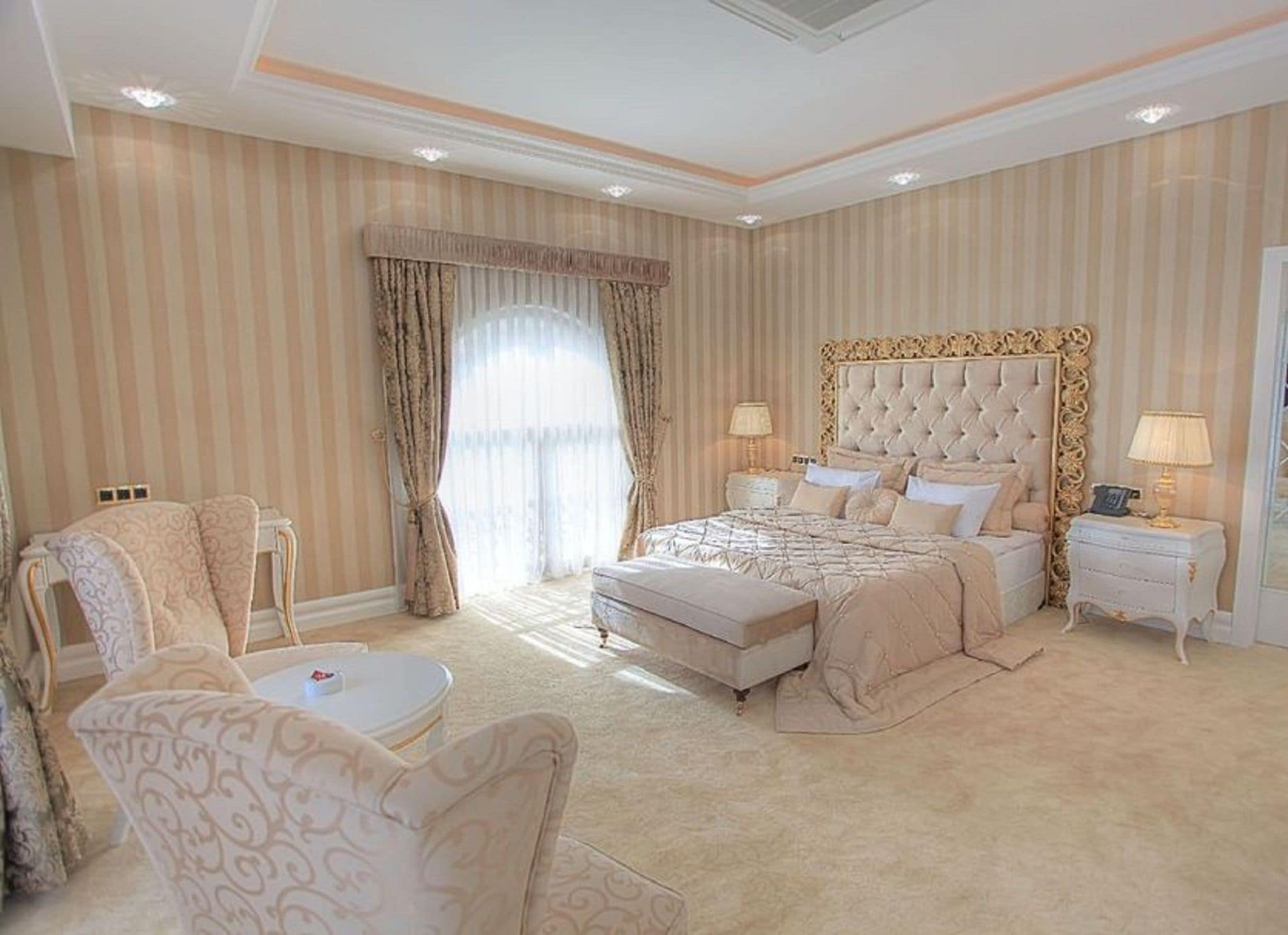 A spacious bedroom with a large bed, a sitting area with a chair, and a nightstand with a lamp.