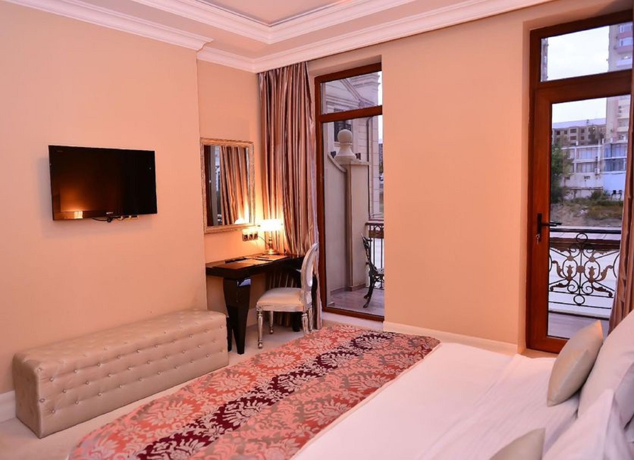 Une chambre d’hôtel comprenant un lit, un bureau, une chaise, une télévision et un balcon avec une rambarde.