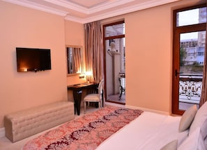 A hotel room with a bed, a desk, a chair, a television, and a balcony with a railing.
