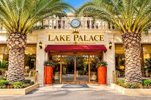 The entrance of Lake Palace with a clock, palm trees, and a red awning.