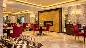 Un lobby de hotel lujoso con un tablero de ajedrez, sillones rojos suaves, una chimenea y una decoración elegante.