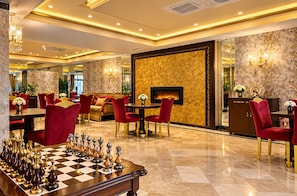 A luxurious hotel lobby with a chessboard, plush red chairs, a fireplace, and elegant decor.