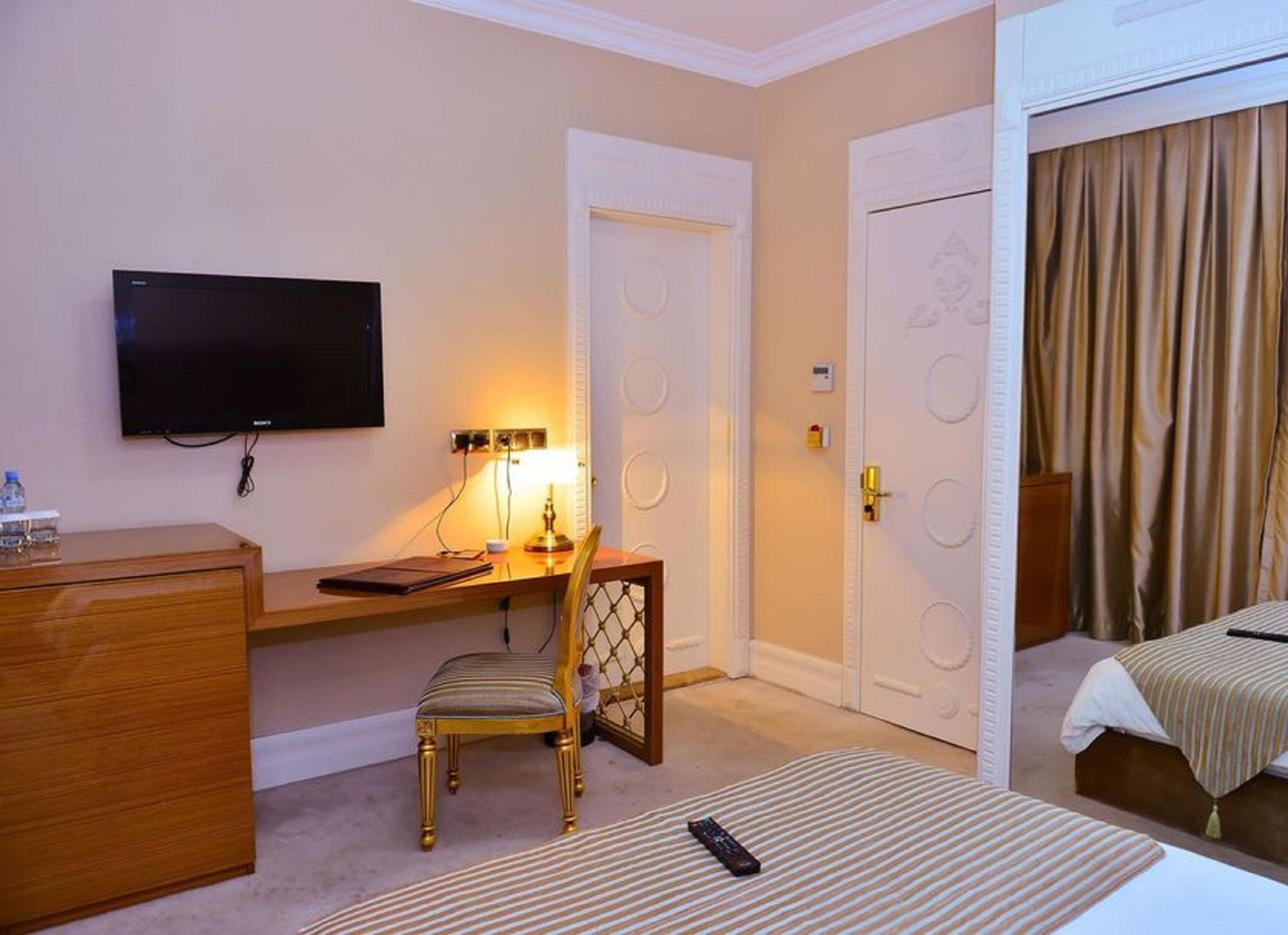 A hotel room with a bed, a desk with a chair, a television, and a door with a curtain.