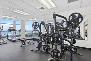 A gym with various exercise equipment, a treadmill, and a view of the beach. - Palacio 603 (Pensacola)