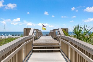 A wooden boardwalk leading to a beach with a flagpole displaying two flags. - Palacio 603 (Pensacola)