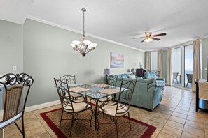 A dining area with a glass table and metal chairs, a sofa set, a ceiling fan, and a view through the glass door. - Palacio 603 (Pensacola)