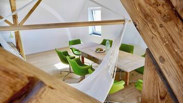 Quarto com estrutura de teto em madeira, uma mesa com cadeiras e uma janela.