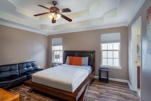 A bedroom with a bed, a black leather couch, a wooden floor, and a ceiling fan. - Quiet neighborhood home with private patio, free parking & easy airport access (Nashville)