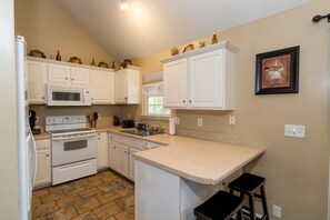 A compact kitchen with white cabinets, a microwave, an oven, a sink, and a small bar stool. - Quiet neighborhood home with private patio, free parking & easy airport access (Nashville)
