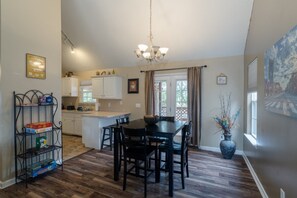 Een eetruimte met een houten tafel en stoelen, een kroonluchter en uitzicht op het omliggende landschap door een raam.