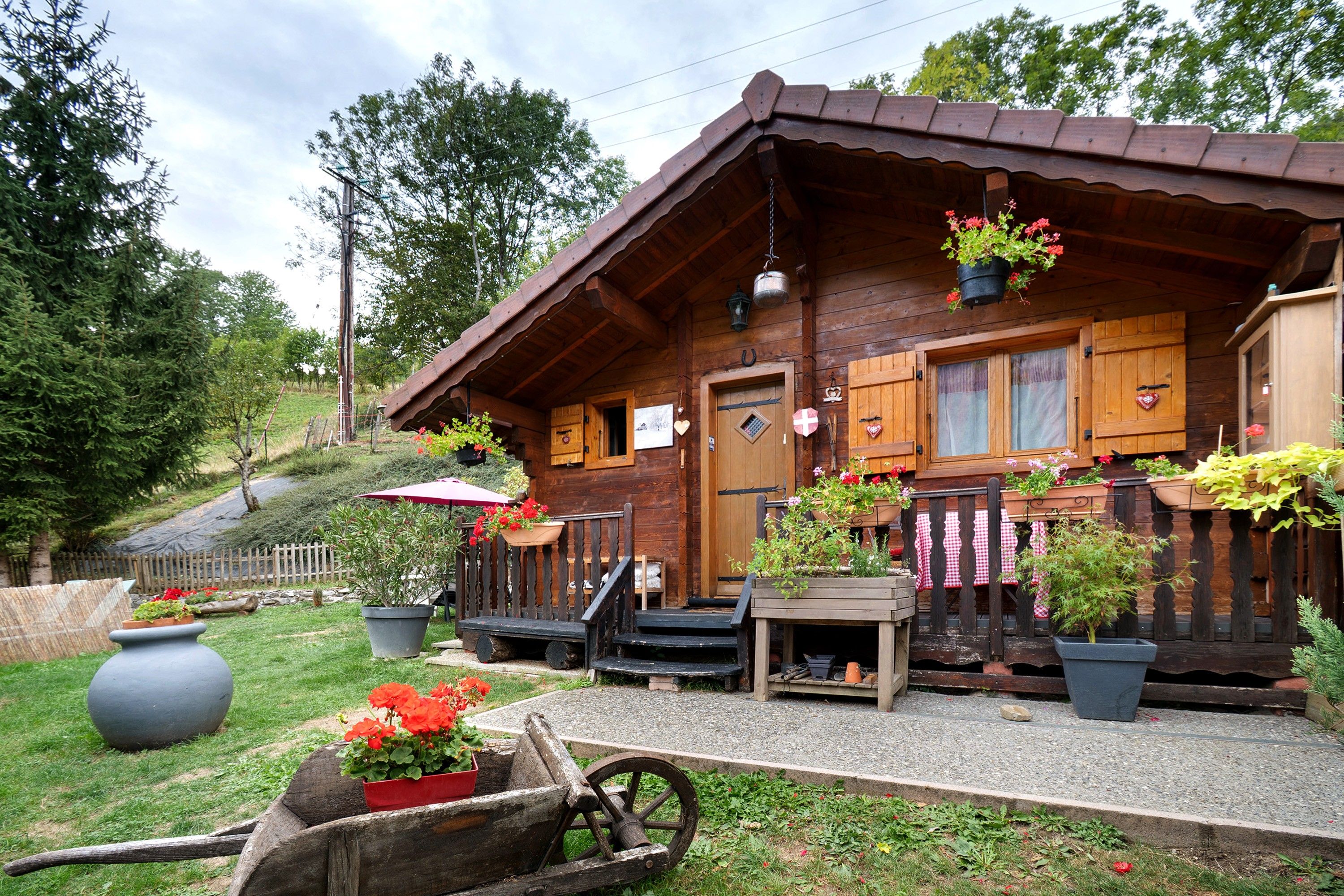 Eine Holzhütte mit Veranda, Blumentöpfen und einem Holzwagen.