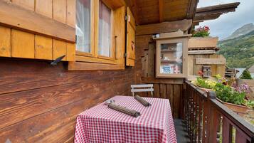 Ein Holzbalkon mit einer karierten Tischdecke, einer Metallschüssel und einem gewebten Gegenstand auf einem Tisch.