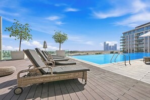 A rooftop pool area with lounge chairs and a view of the city skyline. - Stylish 1BR - Creek Harbour - Pool, Gym & Parking (Dubai)
