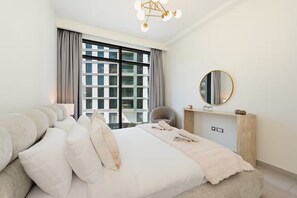 A modern bedroom with a large bed, a window with curtains, a round mirror, and a light fixture. - Stylish 1BR - Creek Harbour - Pool, Gym & Parking (Dubai)