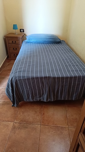 A bed with a striped bedspread, a nightstand with drawers, a lamp, and a wall socket.