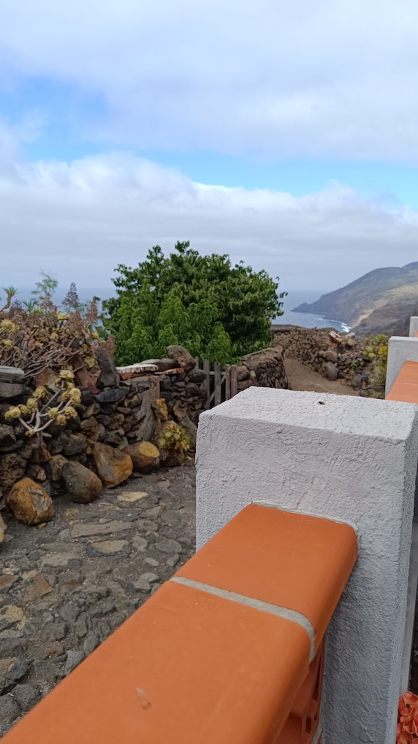 A stone wall with a stone pathway leading to a seating area with orange cushions.
