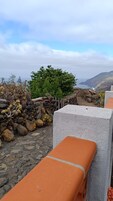 Un muro de piedra con un camino de piedras que lleva a una zona de estar con cojines naranja.