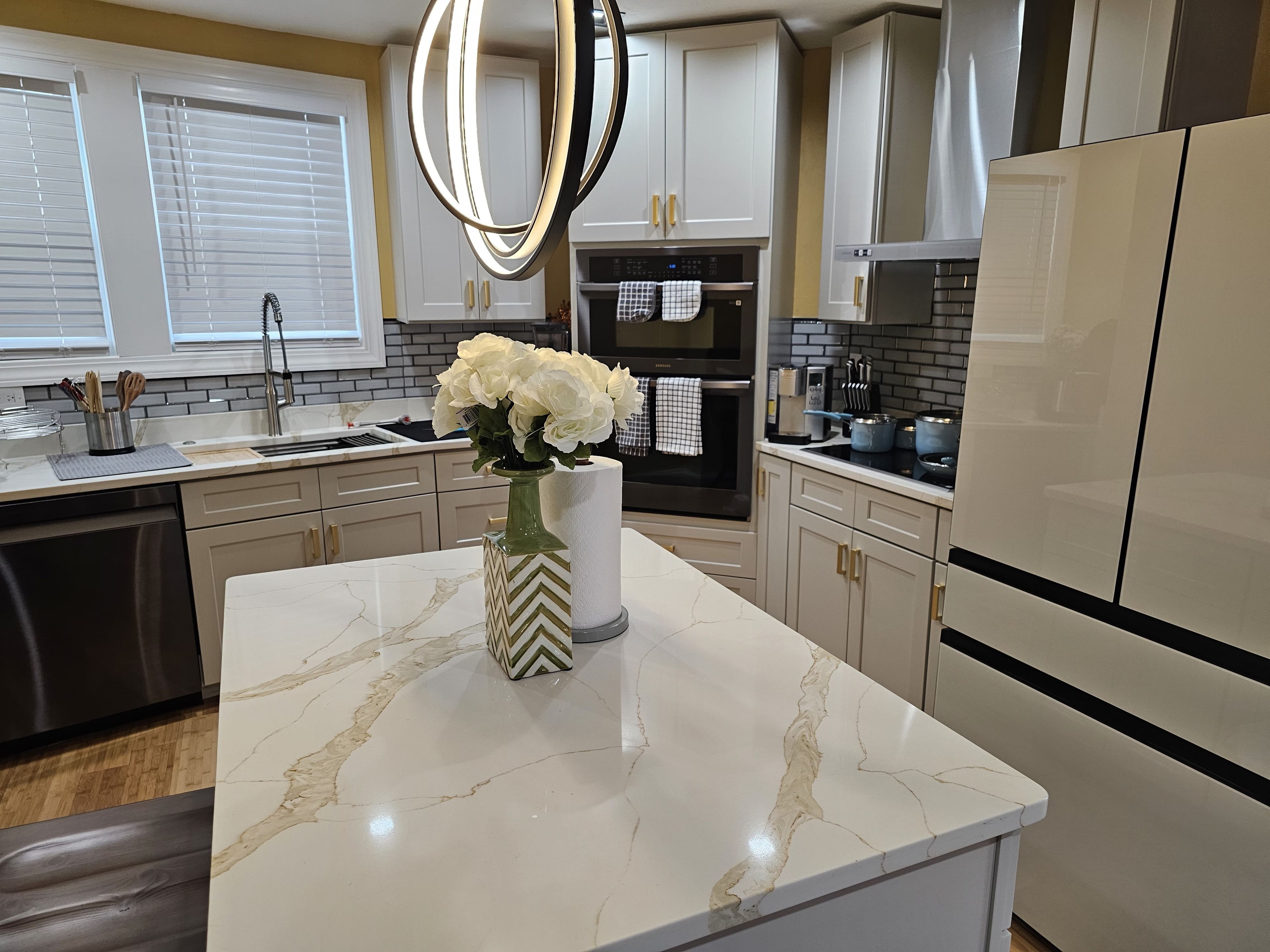 A modern kitchen with marble countertops, stainless steel appliances, and a vase with white flowers on the island.