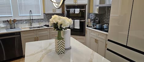 A modern kitchen with marble countertops, stainless steel appliances, and a vase with white flowers on the island.