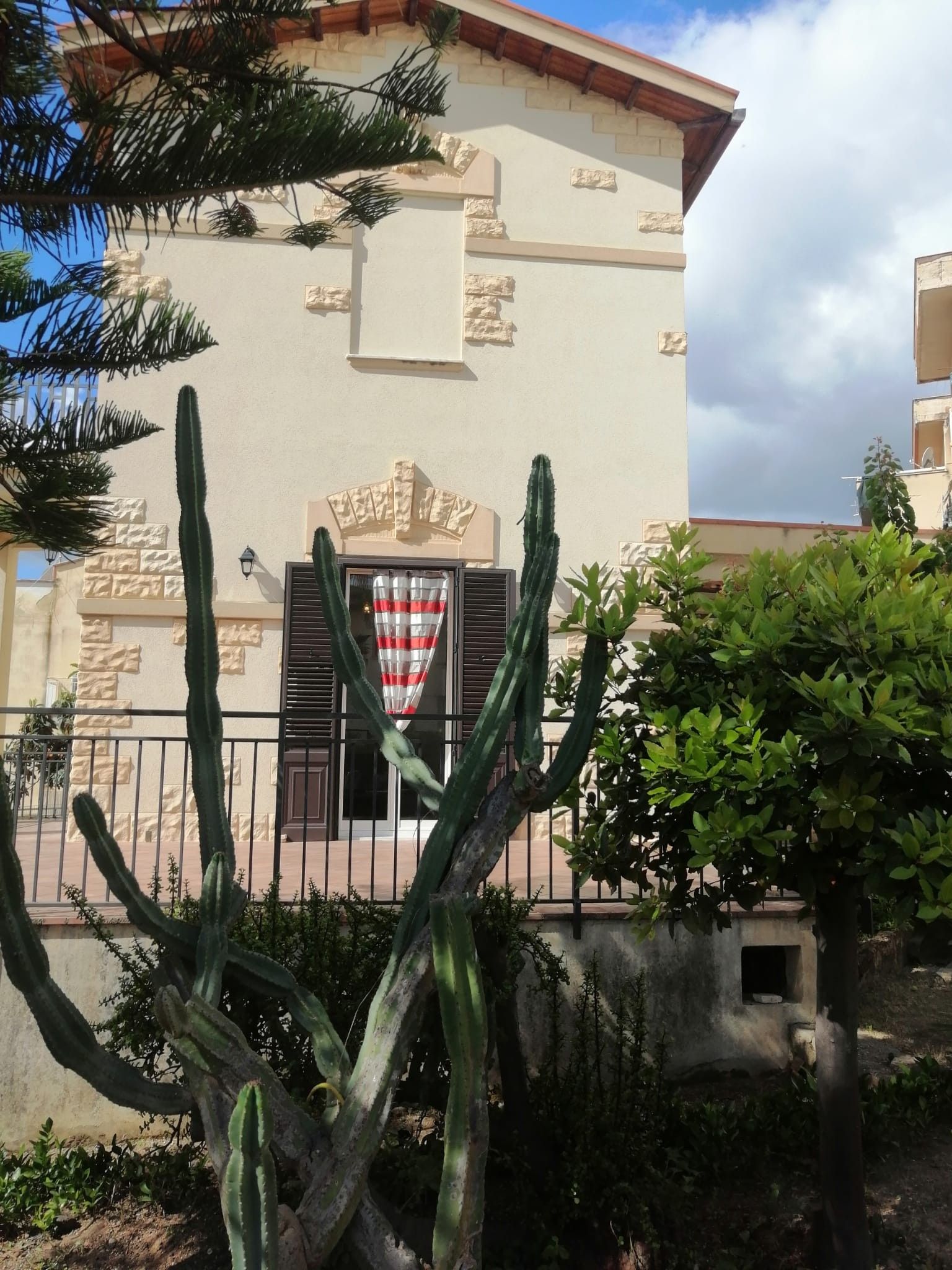 Un bâtiment à la façade en pierre, une fenêtre avec des volets et un cactus au premier plan.