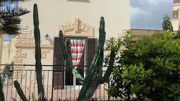 Un bâtiment à la façade en pierre, une fenêtre avec des volets et un cactus au premier plan.