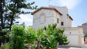 A building with a white facade and a red roof, surrounded by greenery and potted plants.