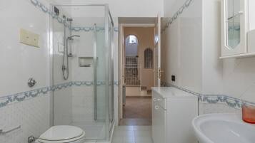 A bathroom with a glass-enclosed shower, a toilet, and a sink.