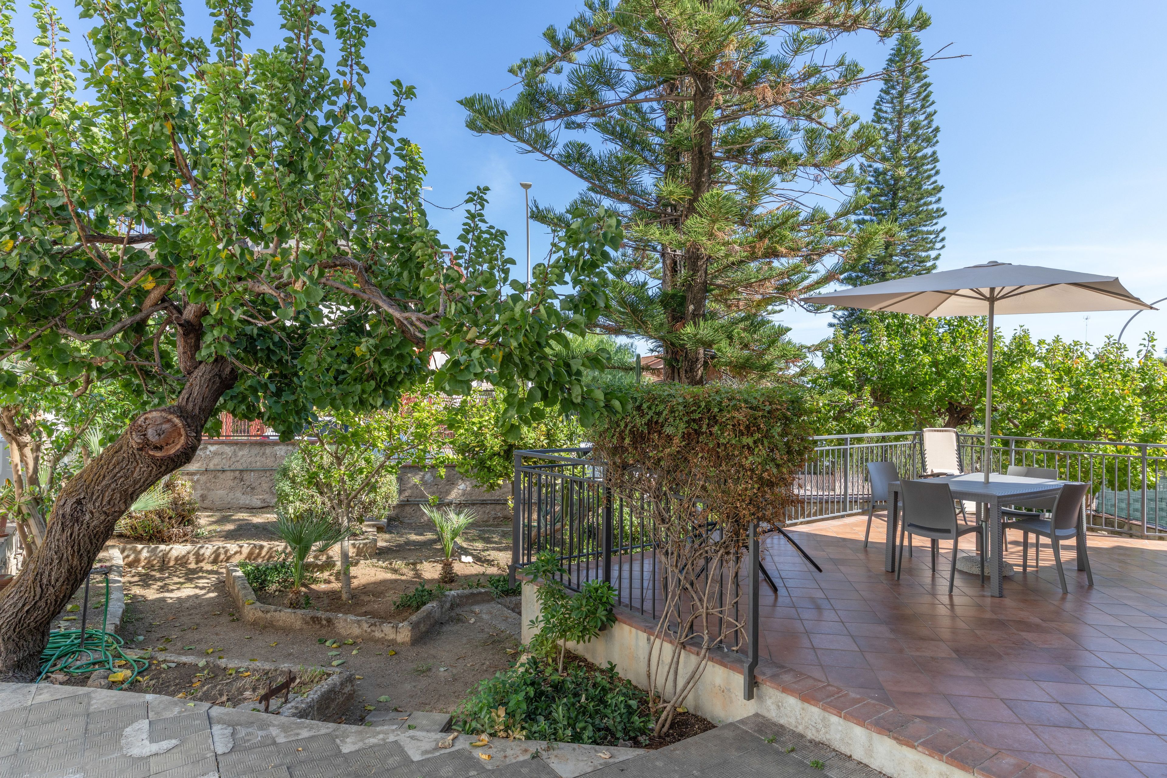 Un espace extérieur aménagé en terrasse, avec une table et des chaises, entouré d’arbres et délimité par une clôture en métal.