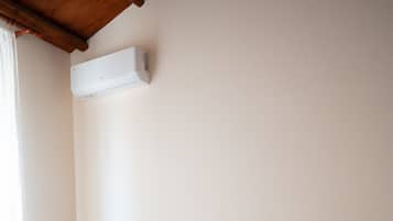 A bedroom with a bed, a white headboard, a wall-mounted air conditioner, and a nightstand.