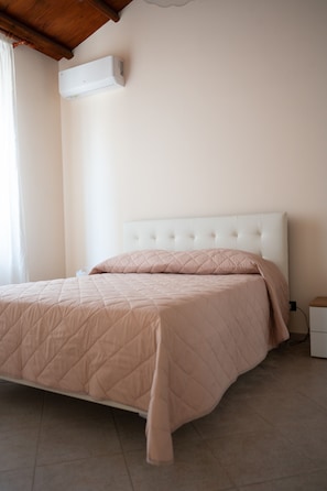 A bedroom with a bed, a white headboard, a wall-mounted air conditioner, and a nightstand.