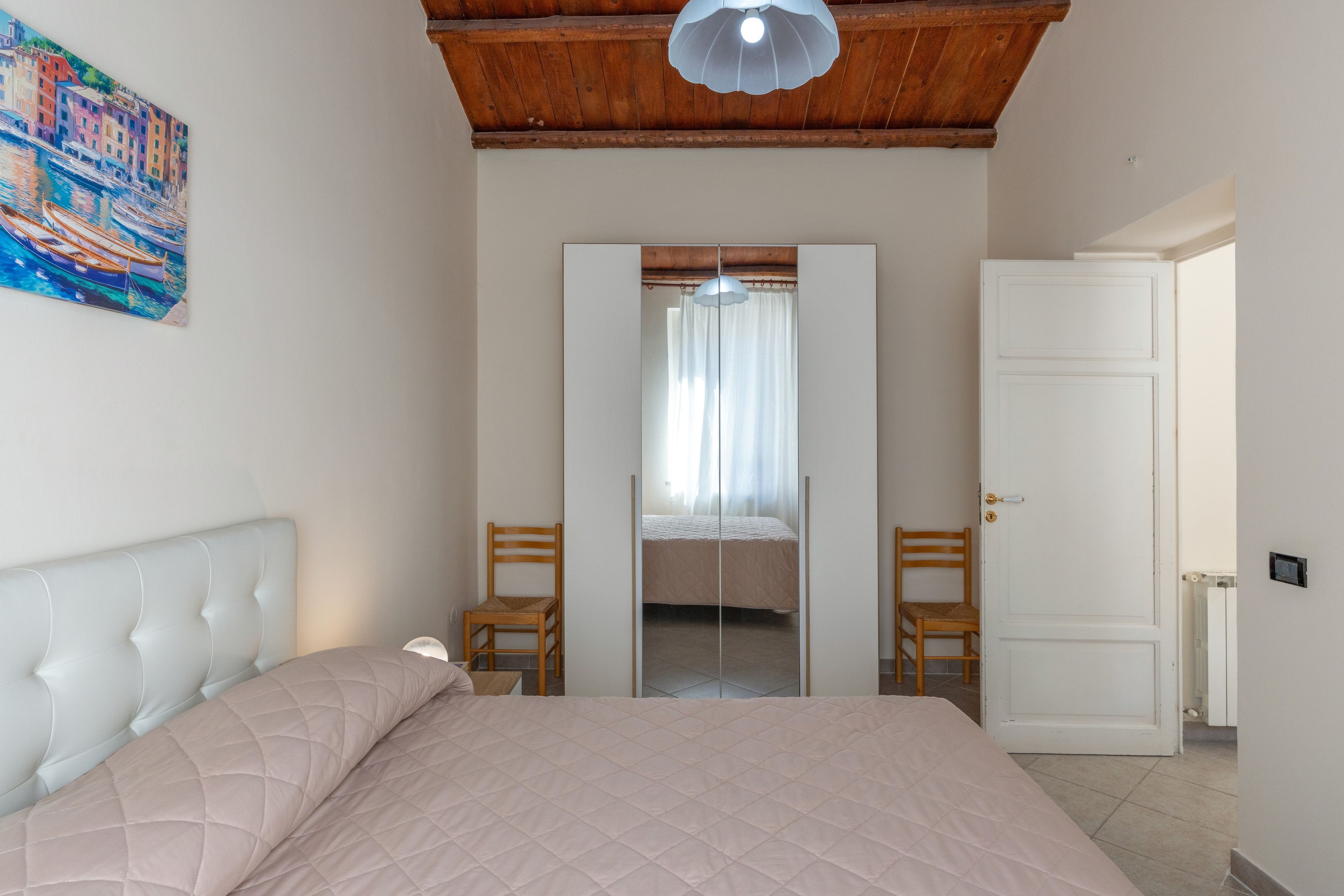A bedroom with a bed, a chair, a wardrobe, and a door.