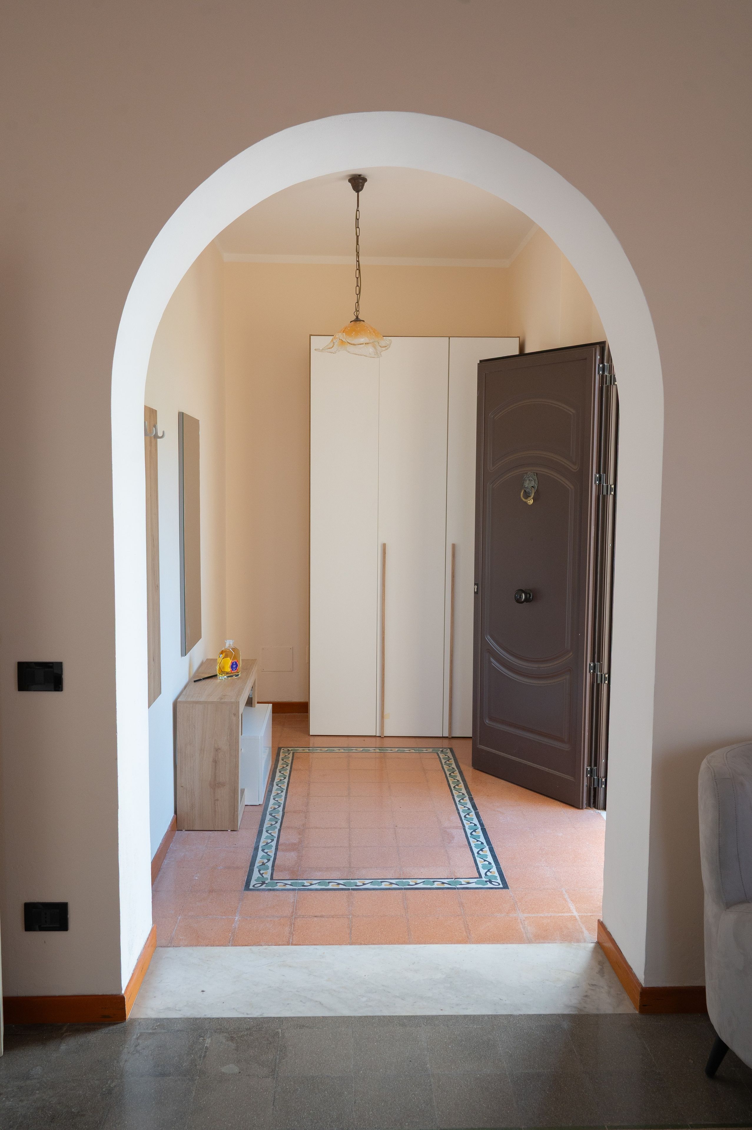 A hallway with a white door, a coat rack, and a hanging light fixture.