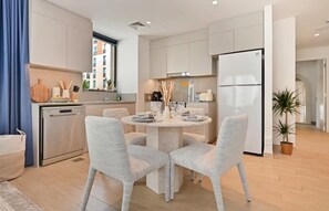 A modern kitchen with a dining area, stainless steel appliances, and a view of the city. - Breeze 2BR - Lagoon & Canal View - Creek Beach (Dubai)