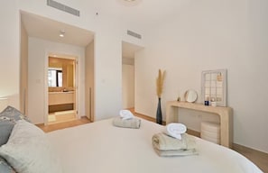 Une chambre d’hôtel avec un lit, une table de chevet, un miroir et une salle de bain visible à travers une porte ouverte.