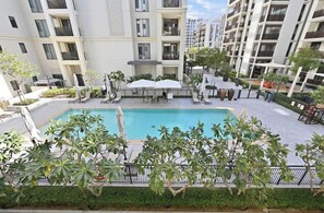 A residential building with a swimming pool surrounded by lounge chairs and umbrellas. - Breeze 2BR - Lagoon & Canal View - Creek Beach (Dubai)