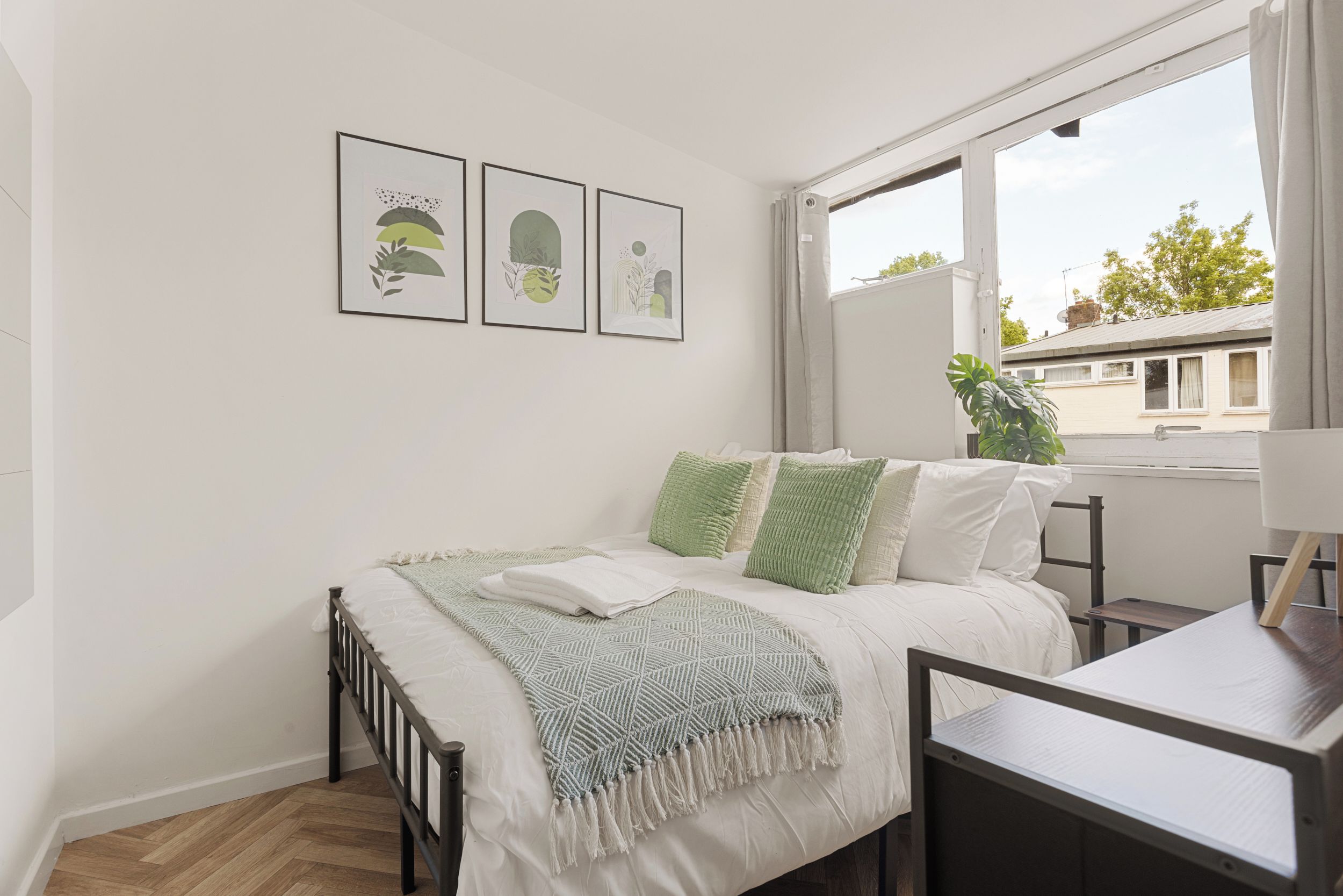 A bedroom with a bed, a nightstand, a window, and three framed artworks on the wall.