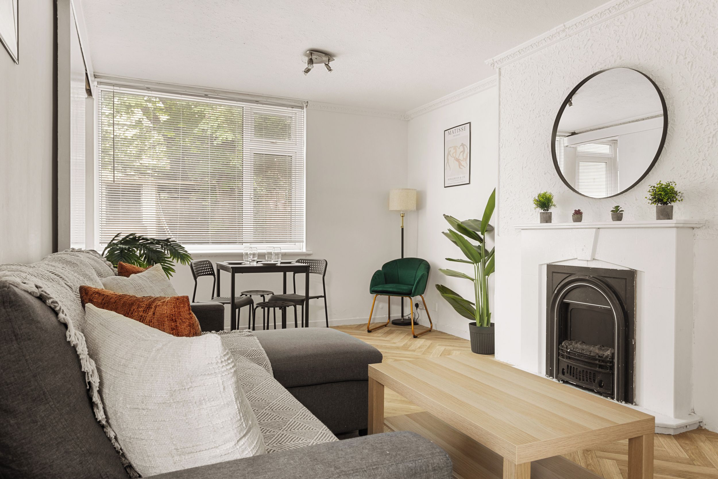 A living room with a sofa, a dining table, chairs, a fireplace, and a large window with blinds.