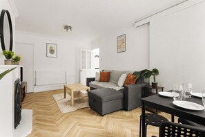 Uma sala de estar moderna com um sofá cinzento, uma mesa de centro de madeira e uma área de jantar com mesa e cadeiras pretas.