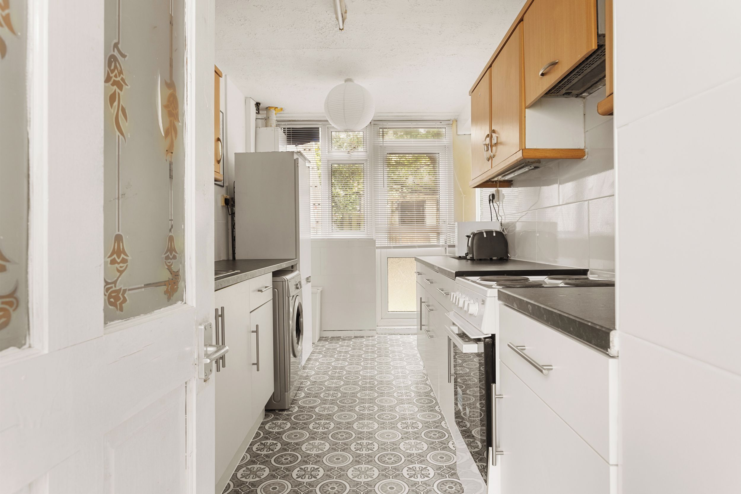 A narrow kitchen with a washing machine, a stove, and a refrigerator.