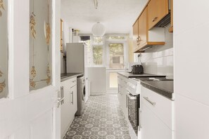 A narrow kitchen with a washing machine, a stove, and a refrigerator. - Forest Hill Base (London)