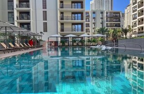 Ein Schwimmbecken mit Liegestühlen und Sonnenschirmen, umgeben von mehrstöckigen Wohngebäuden.